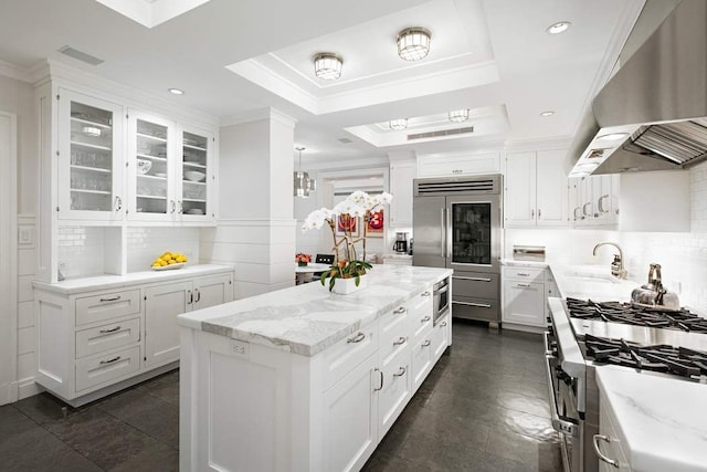 kitchen with extractor fan, white cabinets, premium appliances, a center island, and light stone countertops