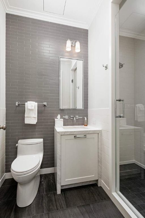 bathroom with tile walls, vanity, an enclosed shower, toilet, and crown molding