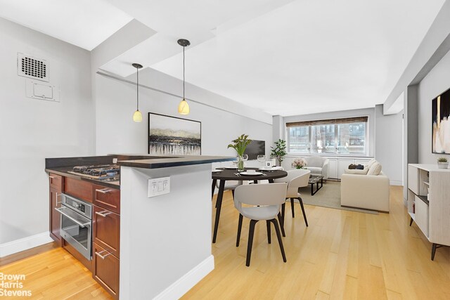 kitchen with appliances with stainless steel finishes, a breakfast bar, hanging light fixtures, kitchen peninsula, and light hardwood / wood-style flooring