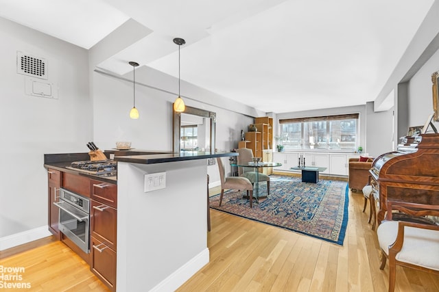 kitchen featuring appliances with stainless steel finishes, a breakfast bar, hanging light fixtures, kitchen peninsula, and light hardwood / wood-style flooring