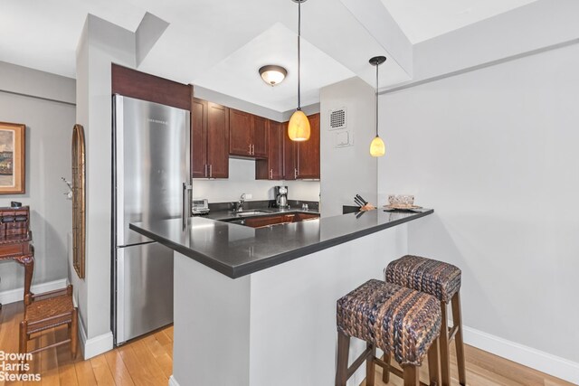 kitchen with dark countertops, a kitchen breakfast bar, decorative light fixtures, a peninsula, and freestanding refrigerator