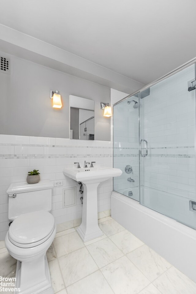 bathroom featuring combined bath / shower with glass door, tile walls, and toilet