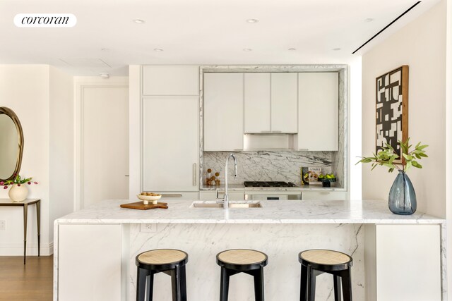 kitchen featuring sink, dark wood-type flooring, backsplash, light stone countertops, and white cabinets