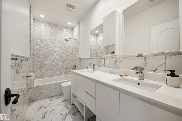 full bathroom with tiled shower / bath, tile walls, vanity, and toilet