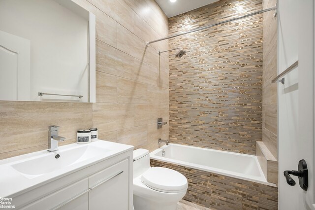 full bathroom featuring toilet, tiled shower / bath, tile walls, vanity, and backsplash