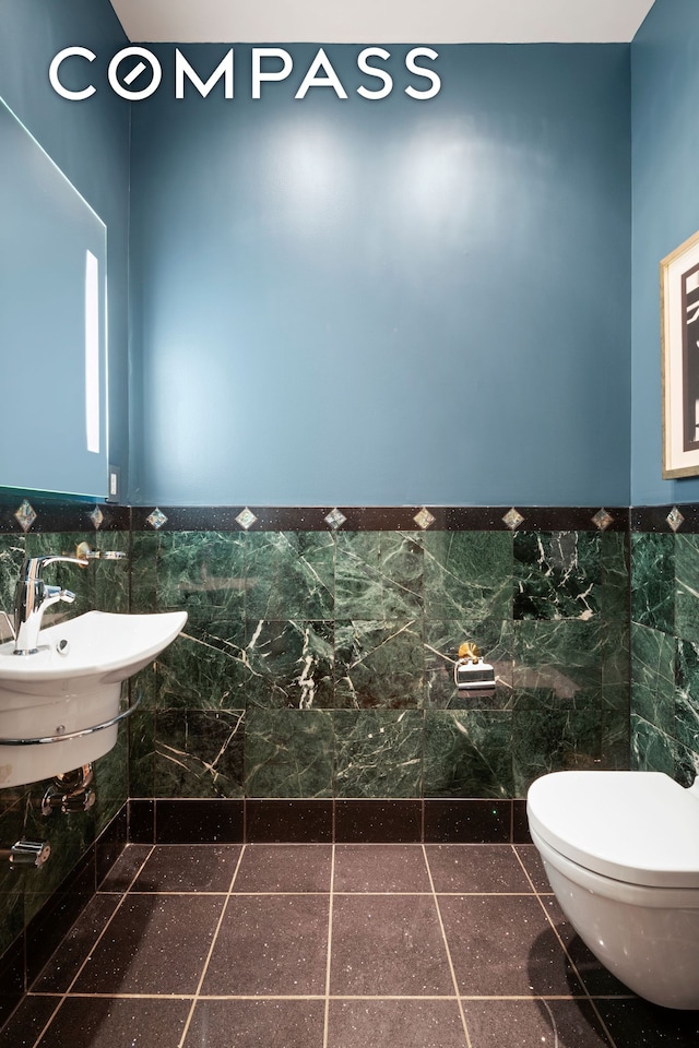 half bathroom with toilet, tile walls, wainscoting, and a sink