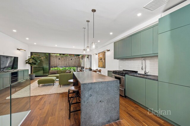 kitchen with sink, stainless steel gas range, hanging light fixtures, dark hardwood / wood-style flooring, and decorative backsplash