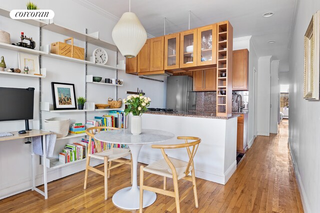 kitchen with crown molding, hanging light fixtures, stainless steel refrigerator, light hardwood / wood-style floors, and backsplash