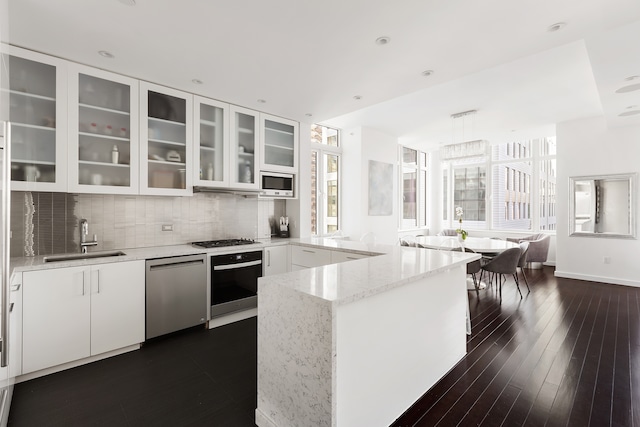 kitchen featuring a sink, light stone countertops, a peninsula, appliances with stainless steel finishes, and white cabinetry