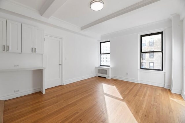 empty room with beam ceiling, light hardwood / wood-style flooring, and built in desk