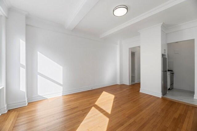 spare room featuring beamed ceiling, ornamental molding, and wood-type flooring