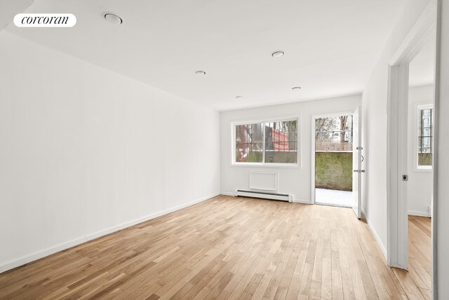 spare room featuring a baseboard heating unit and light hardwood / wood-style floors