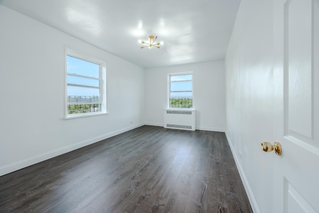 unfurnished room featuring radiator, an inviting chandelier, dark wood-style flooring, and baseboards
