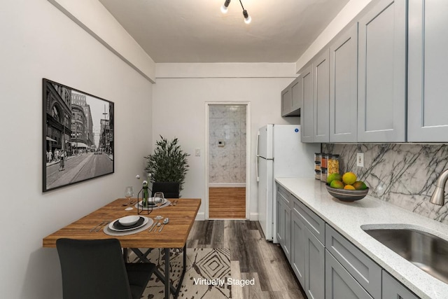 kitchen with sink, gray cabinetry, backsplash, white refrigerator, and wood-type flooring