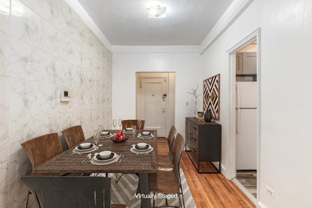 dining room featuring ornamental molding, wood-type flooring, and tile walls