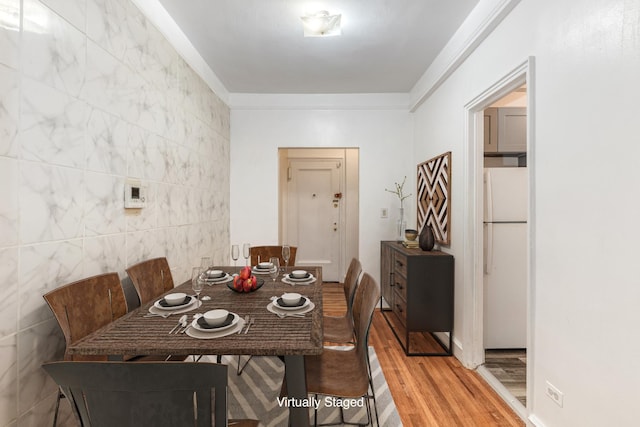 dining space featuring light wood finished floors, tile walls, and ornamental molding