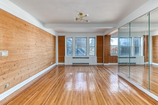 spare room with wood walls, radiator heating unit, baseboards, and wood finished floors