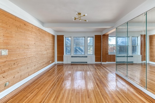 spare room featuring radiator, wood finished floors, a chandelier, and wooden walls