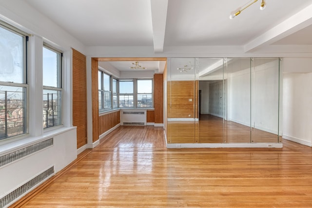 unfurnished room featuring radiator, light wood-style flooring, baseboards, and beamed ceiling