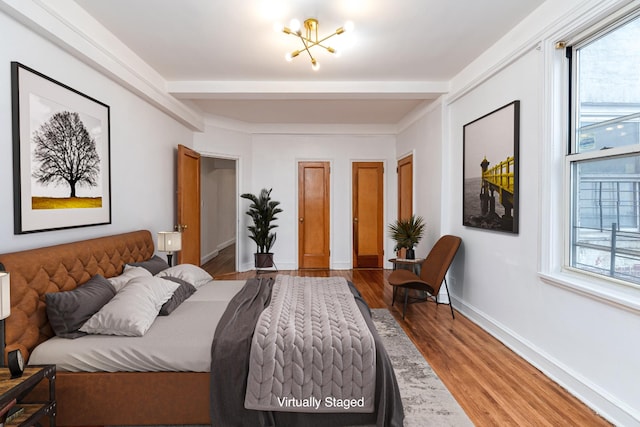 bedroom with beamed ceiling, baseboards, wood finished floors, and multiple windows