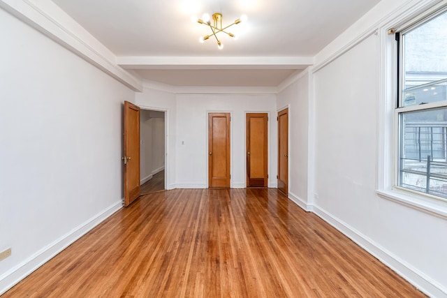 empty room with light wood-type flooring, baseboards, a wealth of natural light, and a notable chandelier