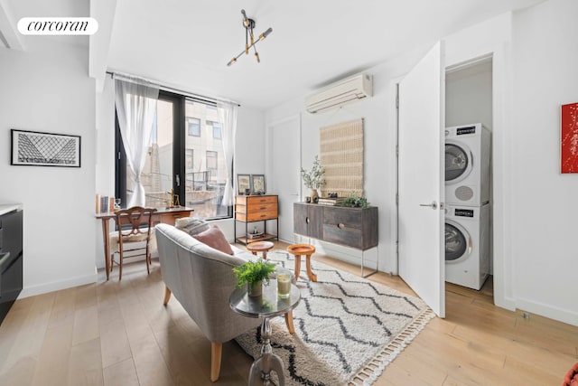 sitting room featuring stacked washing maching and dryer, baseboards, light wood finished floors, and a wall mounted AC