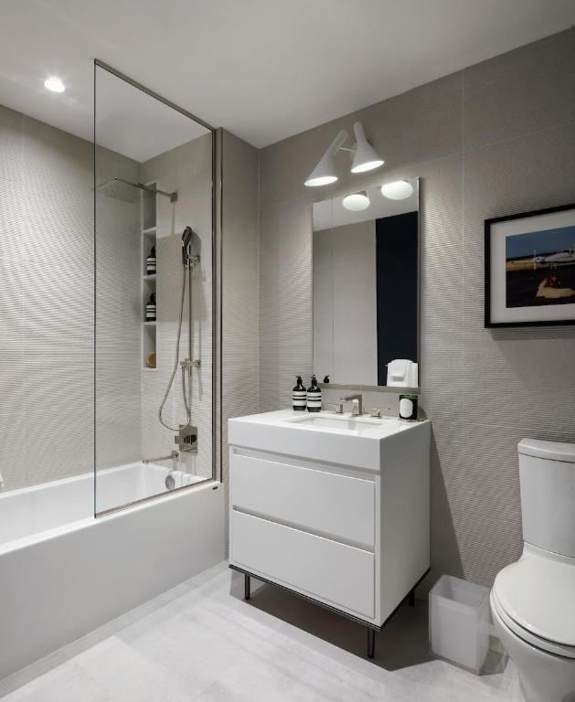 full bathroom with vanity, toilet, tiled shower / bath combo, and tile walls