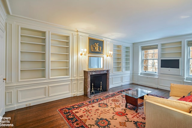 living room with dark hardwood / wood-style flooring, ornamental molding, built in features, and a fireplace