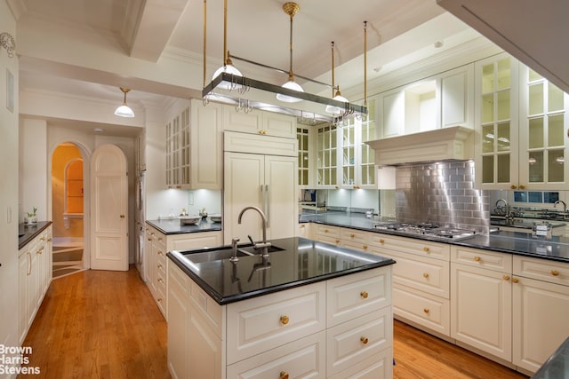 kitchen with stainless steel gas cooktop, sink, hanging light fixtures, paneled built in refrigerator, and a kitchen island with sink