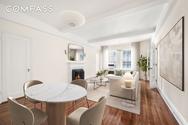 living room with beamed ceiling, baseboards, a lit fireplace, and wood finished floors