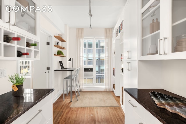 kitchen with glass insert cabinets, white cabinetry, light wood-style flooring, and dark stone countertops