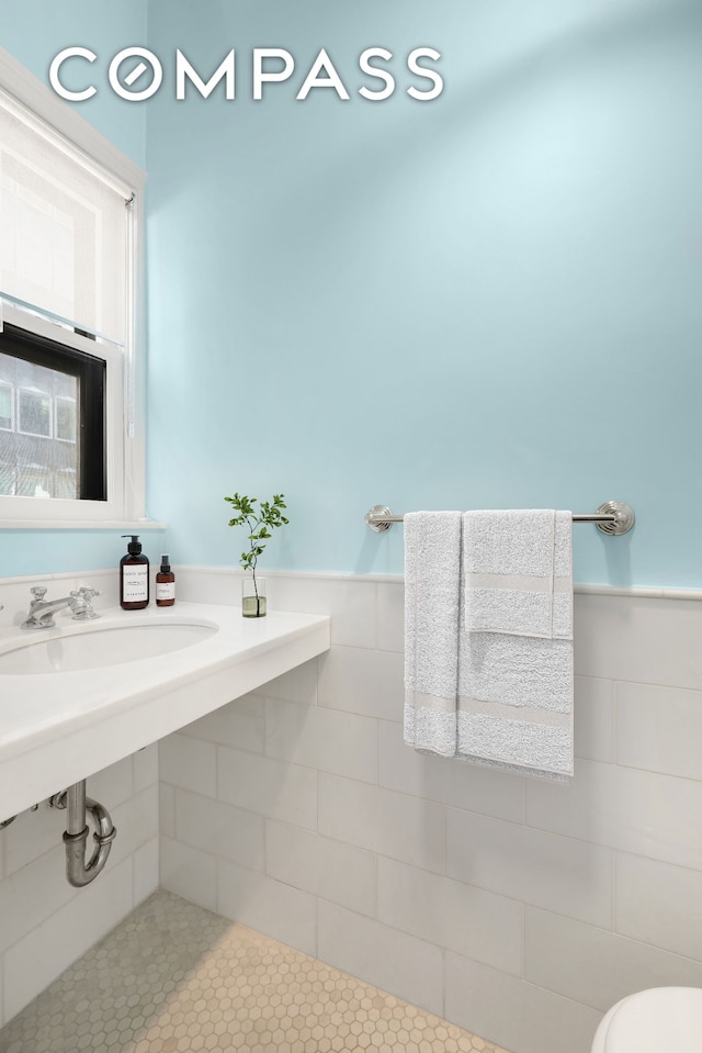 bathroom featuring toilet, wainscoting, a sink, and tile walls