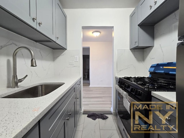 kitchen with marble finish floor, gray cabinets, black gas range, a sink, and light stone countertops