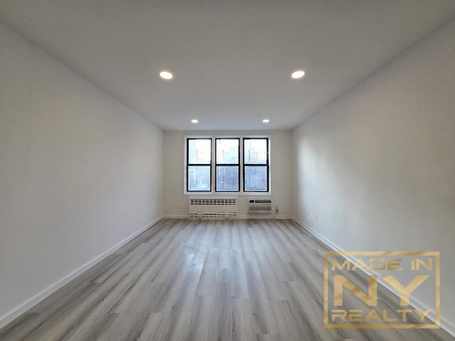 empty room with radiator, light wood-type flooring, baseboards, and recessed lighting