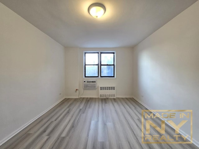 empty room featuring radiator, an AC wall unit, baseboards, and wood finished floors