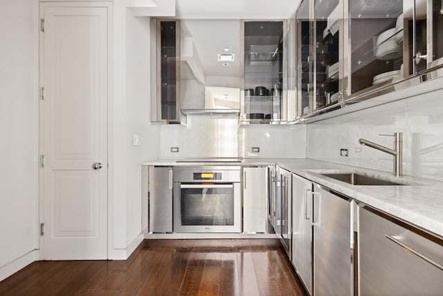 kitchen with light stone countertops, sink, oven, and dark hardwood / wood-style floors