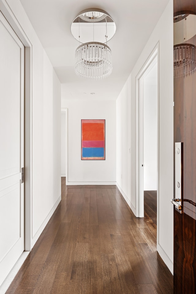 hall featuring dark wood-style floors, baseboards, and a notable chandelier