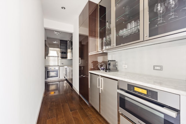 bar featuring premium range hood, stainless steel oven, dark hardwood / wood-style flooring, and light stone countertops