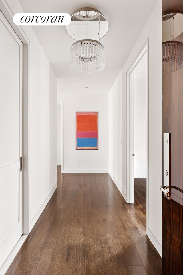 corridor with dark wood-style floors, a notable chandelier, and baseboards