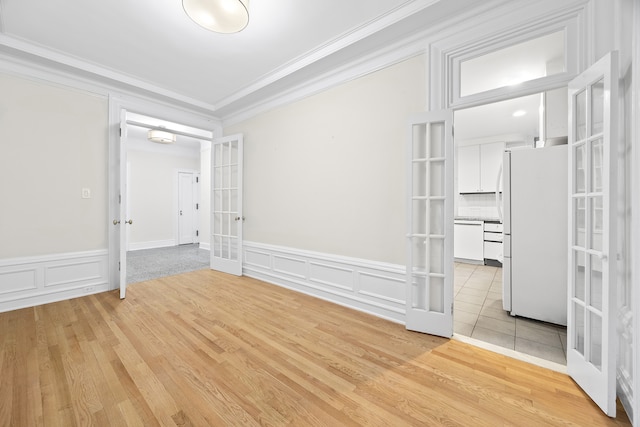 unfurnished room with ornamental molding, french doors, light wood-style floors, wainscoting, and a decorative wall