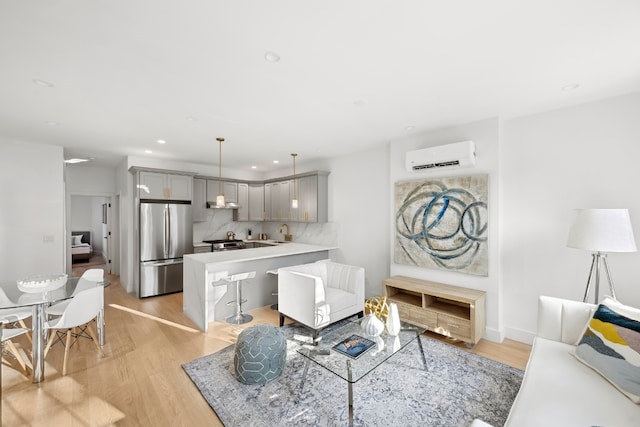 living room with sink, a wall unit AC, and light wood-type flooring