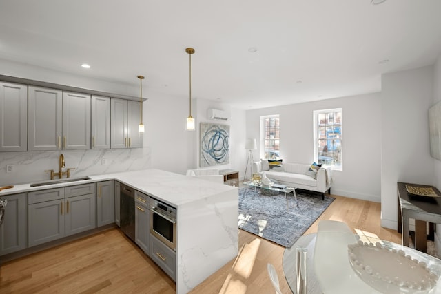 kitchen featuring sink, hanging light fixtures, tasteful backsplash, light hardwood / wood-style floors, and kitchen peninsula