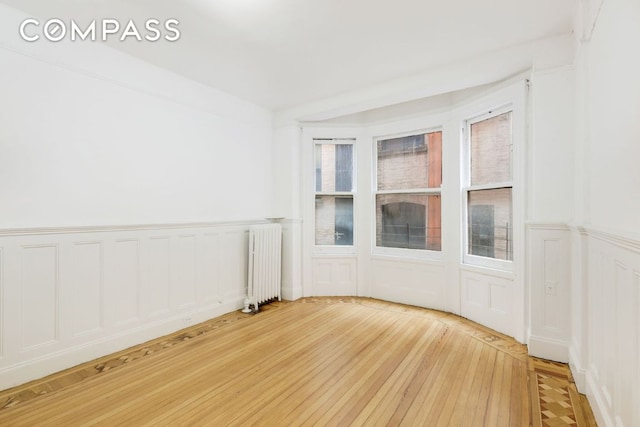 spare room with radiator heating unit and wood-type flooring