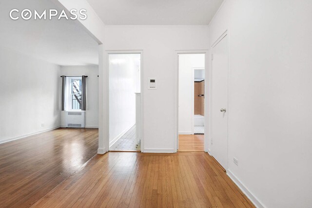 empty room with hardwood / wood-style floors, radiator, and baseboards