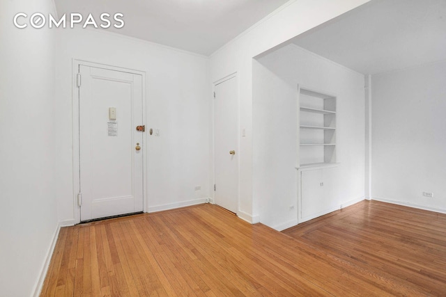 unfurnished room featuring built in shelves, light wood-style floors, baseboards, and ornamental molding