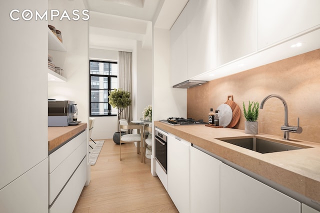 kitchen with decorative backsplash, white cabinets, a sink, stainless steel appliances, and light wood finished floors