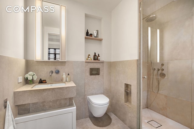 bathroom featuring a walk in shower, a wainscoted wall, toilet, vanity, and tile walls