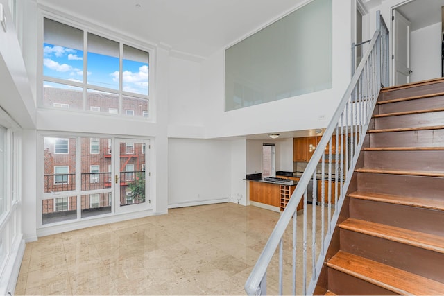 staircase with a baseboard heating unit, a high ceiling, and baseboards