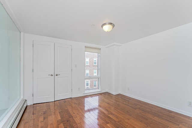 unfurnished bedroom featuring a closet, hardwood / wood-style floors, baseboards, and a baseboard radiator