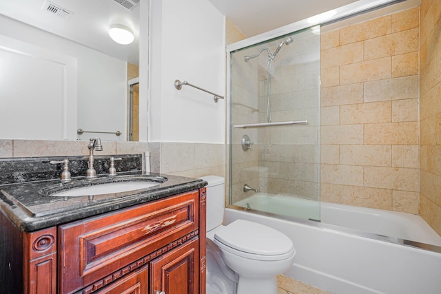 bathroom with visible vents, toilet, shower / bath combination with glass door, tile walls, and vanity